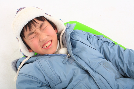 Little Asian boy in winter clothes posing with a green sled - isolated on whiteの写真素材