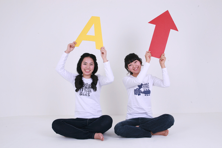 Asian female students holding up an alphabet letter and a red arrow - isolated on whiteの写真素材