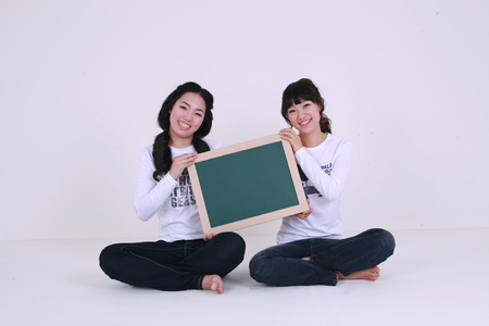 Asian female students holding up a black board together - isolated on whiteの写真素材