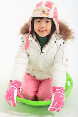 Little Asian girl in winter clothes posing with a green sled - isolated on whiteのeditorial素材