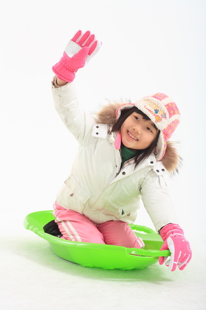 Little Asian girl in winter clothes posing with a green sled - isolated on whiteのeditorial素材