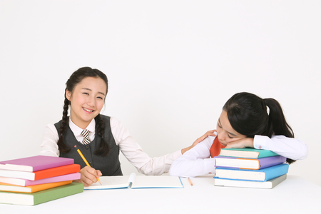 An Asian girl student trying to wake her friend up in the studio, isolated on white.の写真素材
