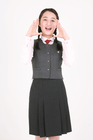 An Asian girl student joining her hands and saying something in the studio, isolated on white.の写真素材