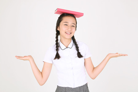 An Asian girl student putting a book on her head in the studio, isolated on white.の写真素材