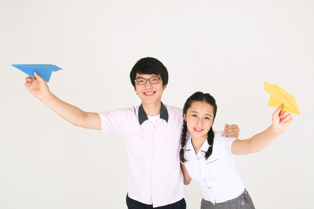An Asian girl and a boy holding a paper airplane in the studio, isolated on whiteの写真素材