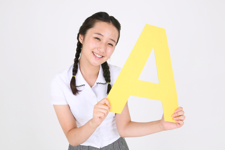 An Asian girl holding an alphabet sign with cute smile in ther studio, isolated on whiteの写真素材