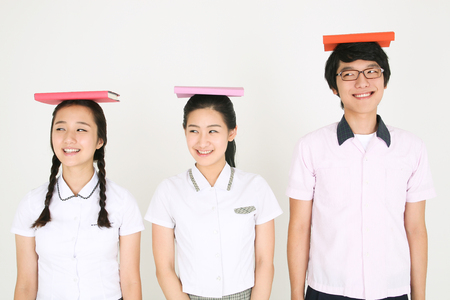 Two Asian girl and a boy standing together and they putting the book on their head in the studio, isolated on white.の写真素材