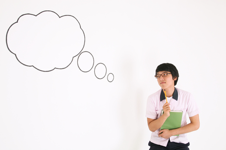 A Asian boy student in front of the speech background holding a book  day dreaming in the studio, isolated on white.の写真素材