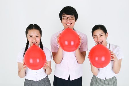 Two Asian girl students and a boy students holding a red balloon in the studio, isolated on white.の写真素材