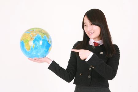 An Asian girl student holding a globe and pointing at it with cute smile in the studio, isolated on white.の写真素材