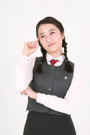 An Asian girl student putting her finger on her head and thinking in the studio, isolated on white.の写真素材