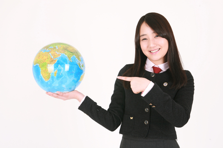 An Asian girl student holding a globe and pointing at it with cute smile in the studio, isolated on white.の写真素材
