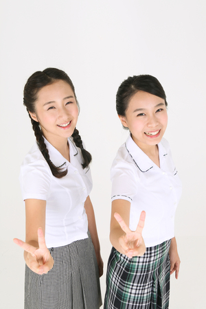 Two Asian girl students standing together and making cute sign with their hands with lovely smile in the studio, isolated on white.の写真素材