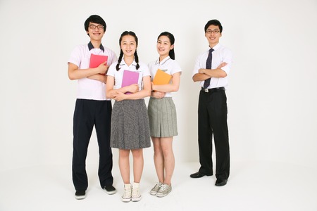 Three students with books and  their teacher crossing arms standing together friendly in the studio, isolated on whiteの写真素材