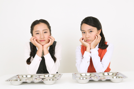 Two Asian girl students waiting for food with bored face in the studio, isolated on white.の写真素材