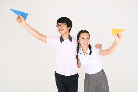 An Asian girl and a boy holding a paper airplane in the studio, isolated on whiteの写真素材