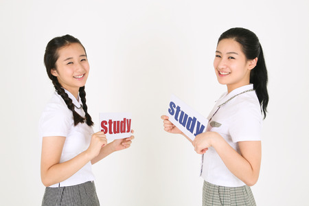 Two Asian girl students facing each other and holding a study sign in the studio, isolated on white.の写真素材