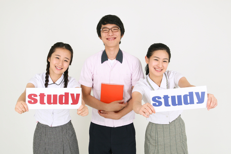 Two Asian girl students holding a study sign and a boy student holding a book in the studio, isolated on white.の写真素材