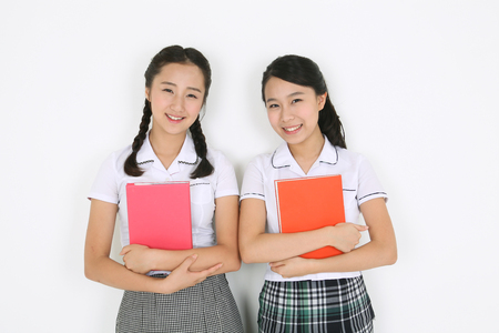 Two Asian girls holding books with their amrs in the studio, isolated on white.の写真素材
