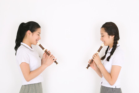 Two Asian girl students facing each other and they playing a recorder in the studio, isolated on whiteの写真素材