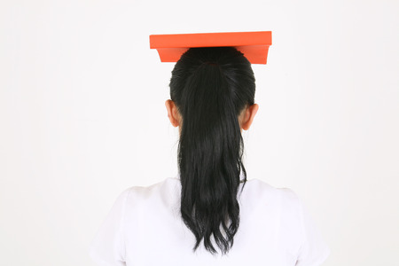 An Asian girl student putting a book on her head and turning back in the studio, isolated on white.の写真素材