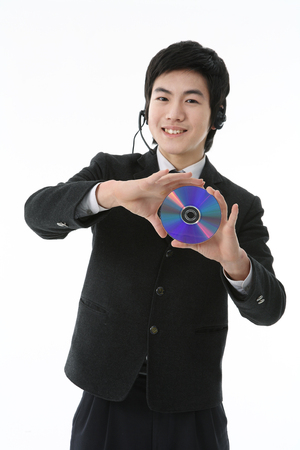 An Asian boy student holding a CD with cheerful smile in the studio, isolated on white.の写真素材