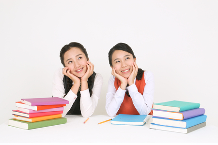 Two Asian girl students sitting behind two stacks of books with smile face in the studio, isolated on white.の写真素材
