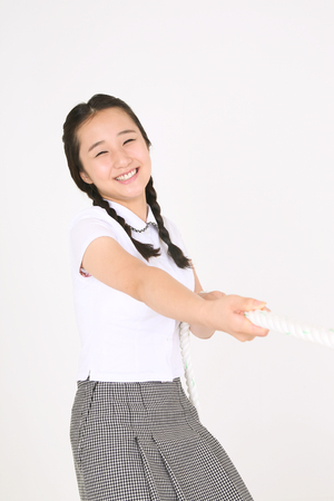 An Asian girl student pulling a rope in the studio, isolated on white.の写真素材