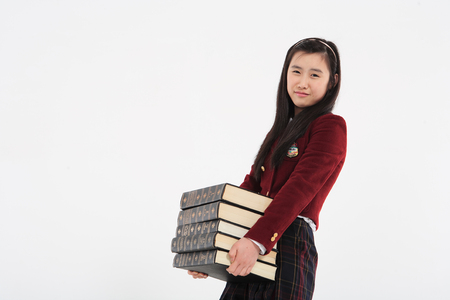 Young Asian girl student with stack of books in the studio, isolated on whiteの写真素材