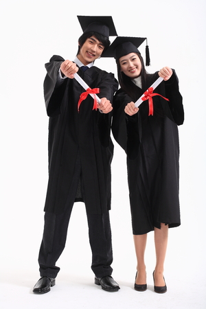 An Asian woman and a man with a graduation hat and clothes in the studio, isolated on whiteの写真素材