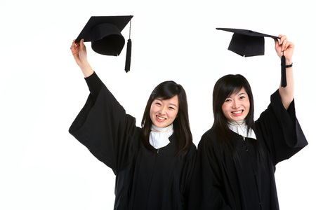 Two Asian women with a graduation hat and clothes in the studio, isolated on whiteの写真素材