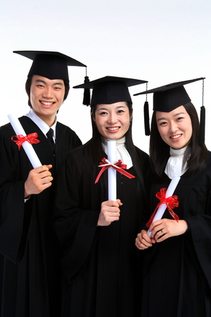 Two Asian women and a man with a graduation hat and clothes in the studio, isolated on white.の写真素材