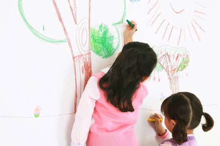 Back view of two Asian girls painting on the wall - isolated on whiteの写真素材