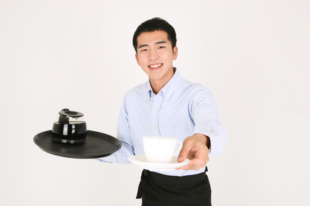 A young man carrying a cup and a coffee potの写真素材
