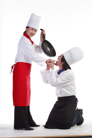 A female cook threatening a male cook with a wokの写真素材