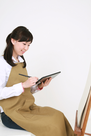 A female artist painting with a brush and a palet as sitting in front of the easelの写真素材