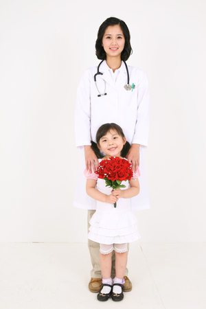 A female doctor holding a young girl patient holding a bouquet of red flowersの写真素材