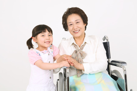 A senior patient sitting in wheelchair holding hands with the grand-daughterの写真素材