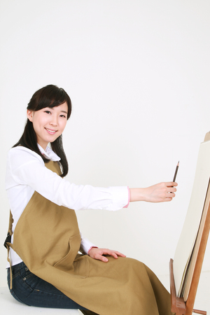 A female artist drawing with a pencil sitting in front of the easelの写真素材