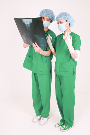 Full shot of A male surgeon and a female surgeon wearing surgery masks looking at an x-ray photographsの写真素材
