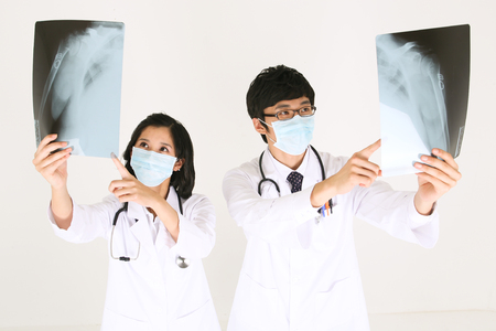 A couple of doctors looking at x-ray photographs as wearing surgery masksの写真素材