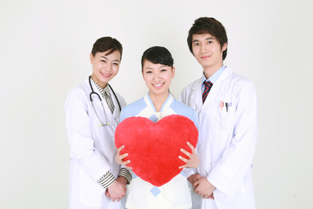 Close up shot of A female nurse holding a heart shaped cushion as standing between a male doctor and a female doctorの写真素材