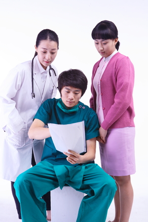 A female doctor and nurse talking standing behind the male surgeon sitting down on chairの写真素材