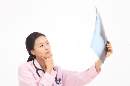 Close up shot of A female doctor in pink robe putting a hand on chin as holding an x-ray photographの写真素材