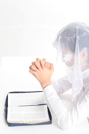 Close up shot of Side shot of a female Asian praying with folded hands in front of the open bible as wearing mass veilの写真素材