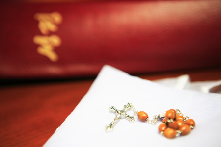 Close up shot of a brown rosary laid on the folded white mass veil with the bible in the backの写真素材