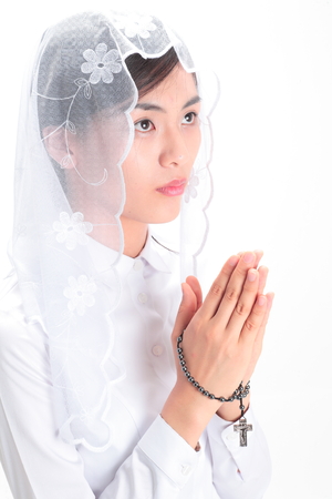 Close up shot of A female Asian wearing a mass veil praying as holding a rosary in handの写真素材