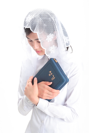 Isolated shot of a female Asian's hands with a rosary ring holding the bible tightlyの写真素材