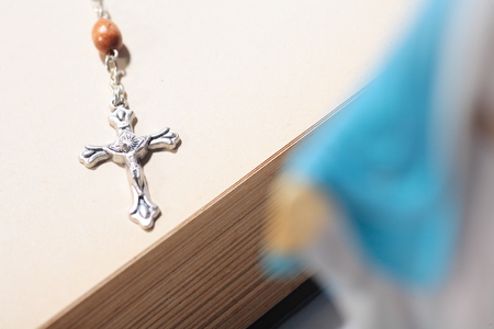 Isolated shot of the cross of rosary behind the table statue of virgin Mary