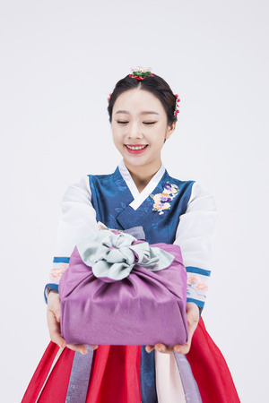 Young Asian woman in Hanbok, Korean traditional clothes, posing with a gift - isolated on whiteの写真素材